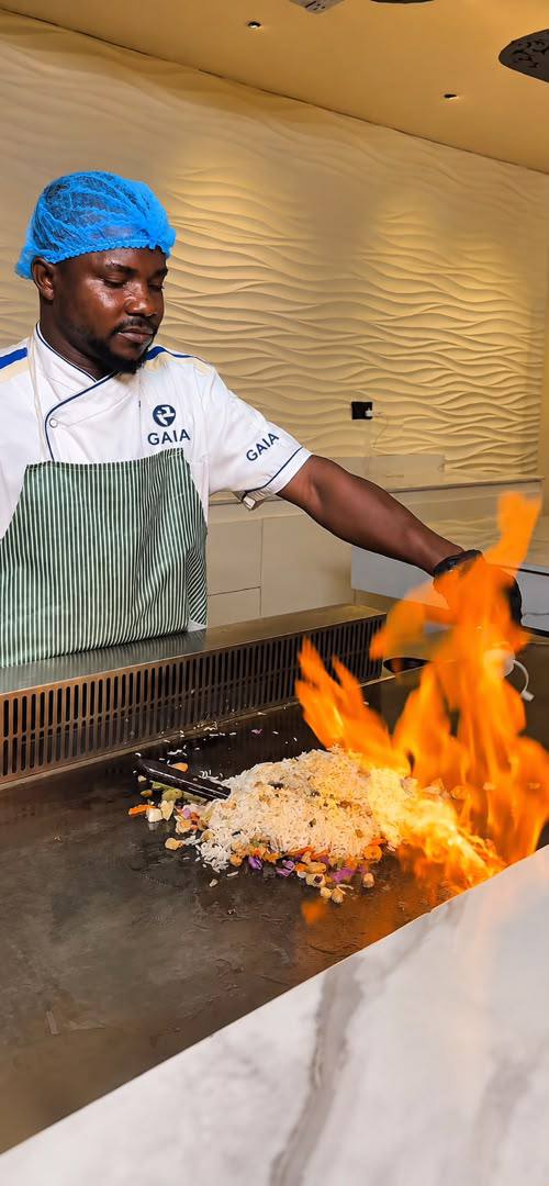 A GAIA HOTELS & SUITES chef finishing a flambé dish at the live cooking station